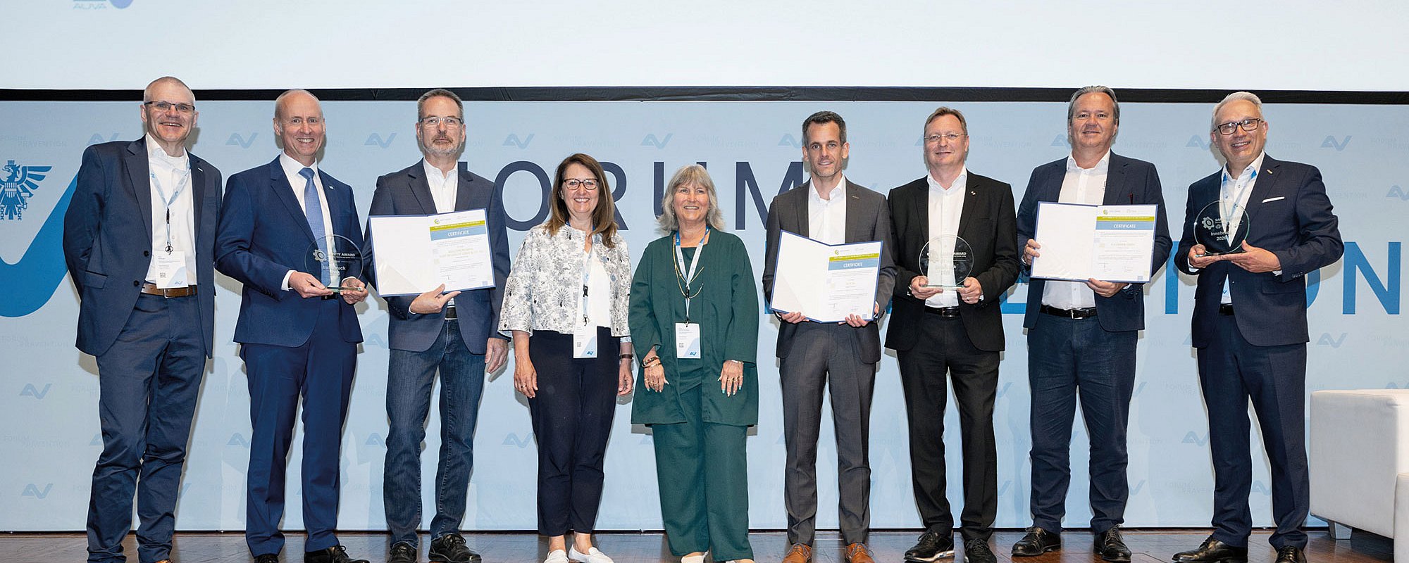 #htmlcaption-10 Foto: Mehrere Preisträgerinnen und Preisträger stehen gemeinsam auf einer Bühne und präsentieren Urkunden sowie Auszeichnungen. Die feierliche Gruppenaufnahme dokumentiert eine Preisverleihung im Rahmen einer professionell organisierten Fachveranstaltung.