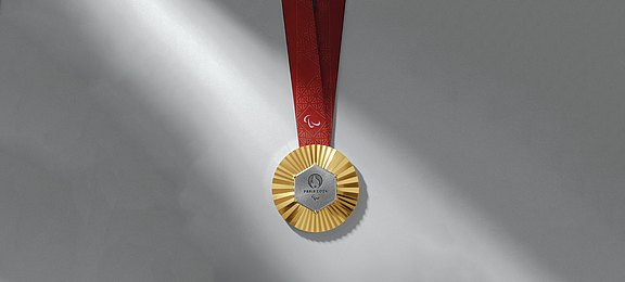 Foto: Goldmedaille der Paralympischen Spiele 2024 mit einem Stück Eiffelturm in der Mitte 